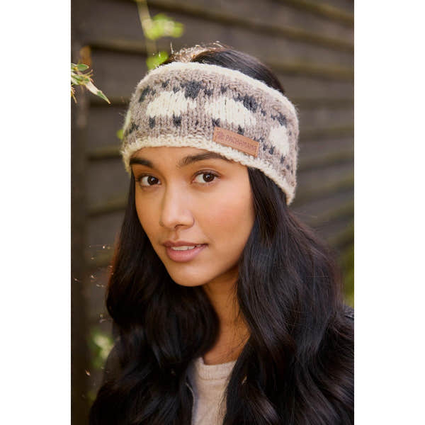 Pachamama Merino sheep headband with mushroom pattern, knit fabric, tan and gray colors, featuring a leather logo tag, worn by a woman outdoors.