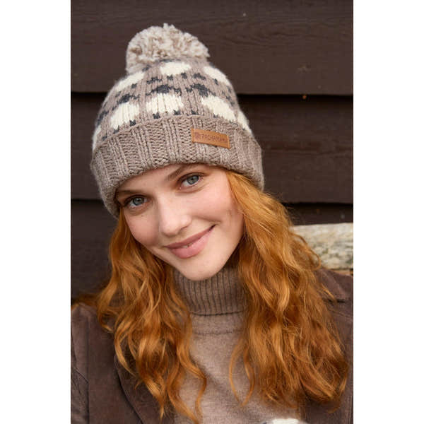 Woman wearing a Pachamama Merino sheep roll-back beanie with plush pom-pom, mushroom pattern, and tan leather tag.
