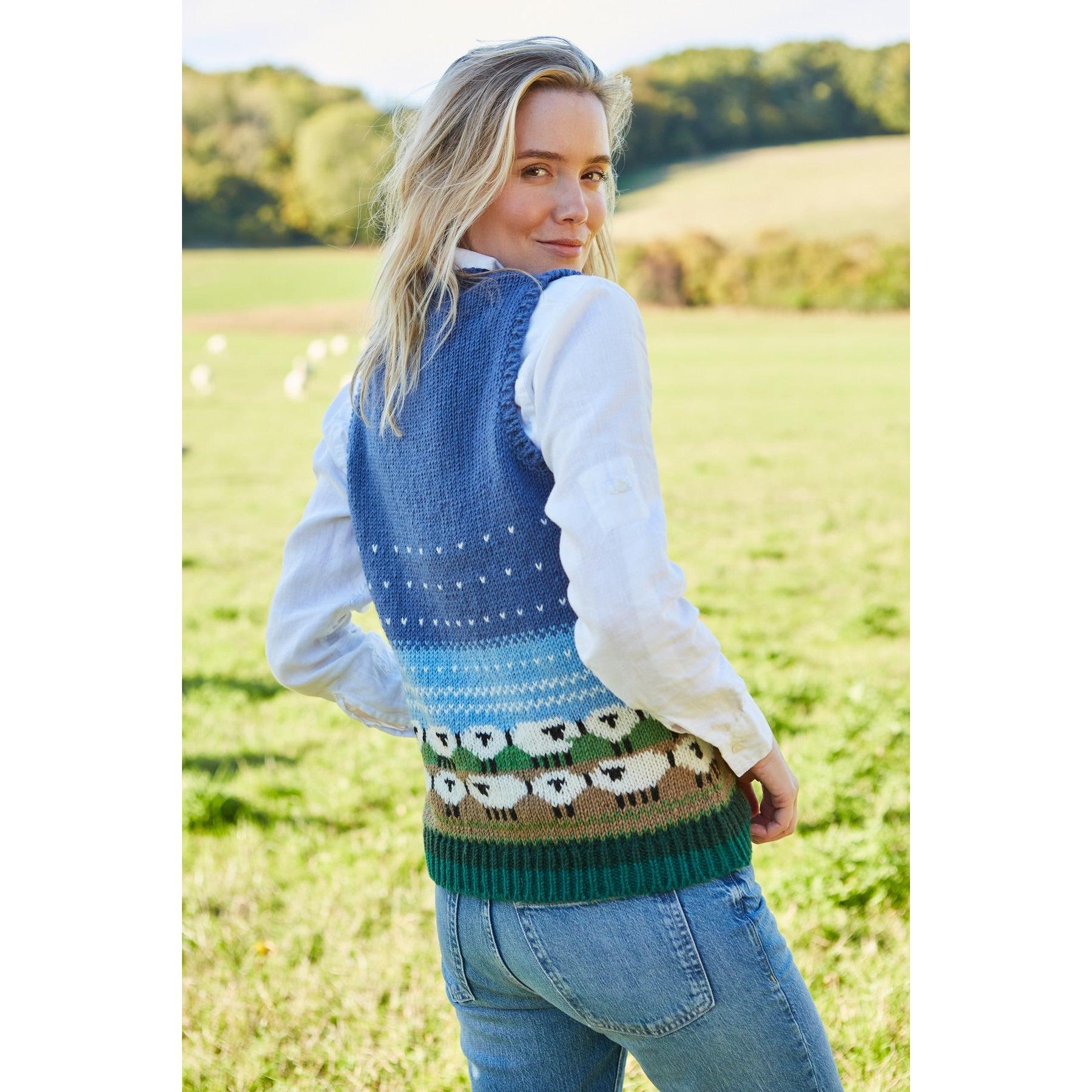 Pachamama snowy sheep patterned tank top with blue gradient background, worn over a white shirt, outdoors in a green field.