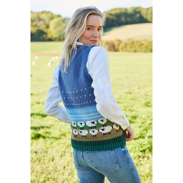 Pachamama snowy sheep patterned tank top with blue gradient background, worn over a white shirt, outdoors in a green field.