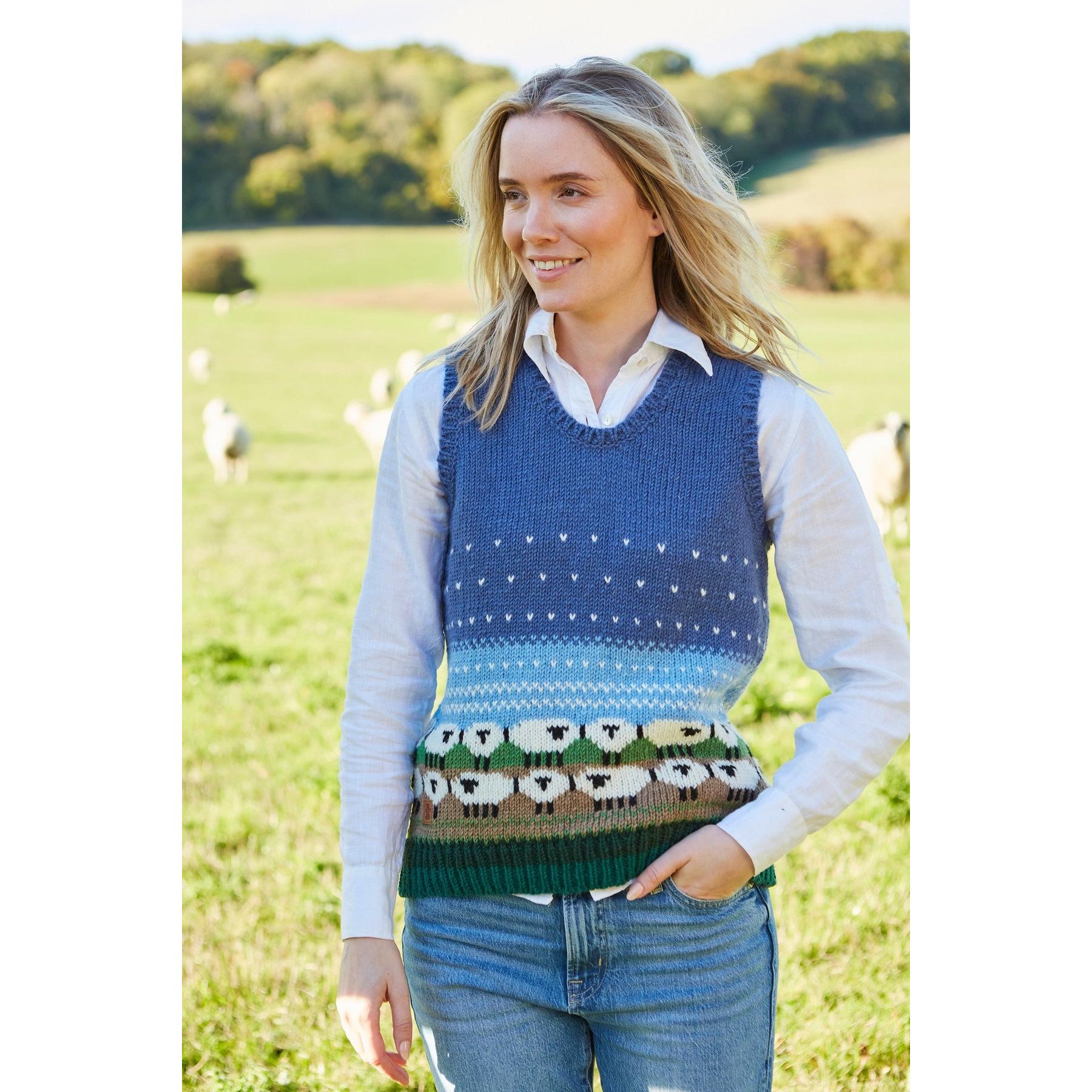 Pachamama Snowy Sheep knit tank top featuring sheep and mountain motifs, layered over a white shirt, in outdoor farm setting.