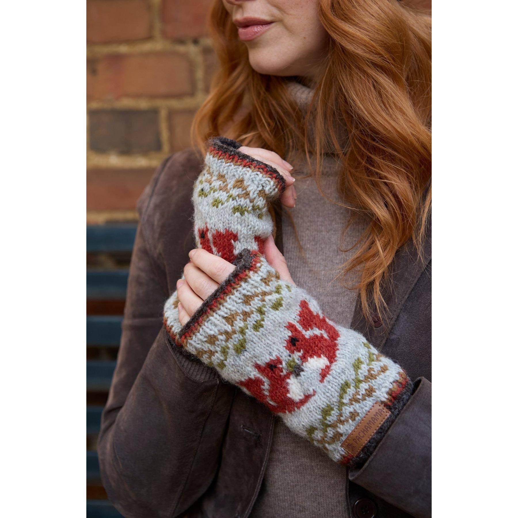 Pachamama Squirrel handwarmer knit gloves with red, green, and white winter pattern, worn by a woman outdoors.