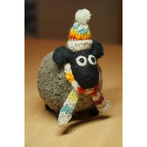 Pachamama Stuart the Lakeland Sheep plush toy with a colorful knitted hat and scarf, made of felt and wool, on wooden surface.