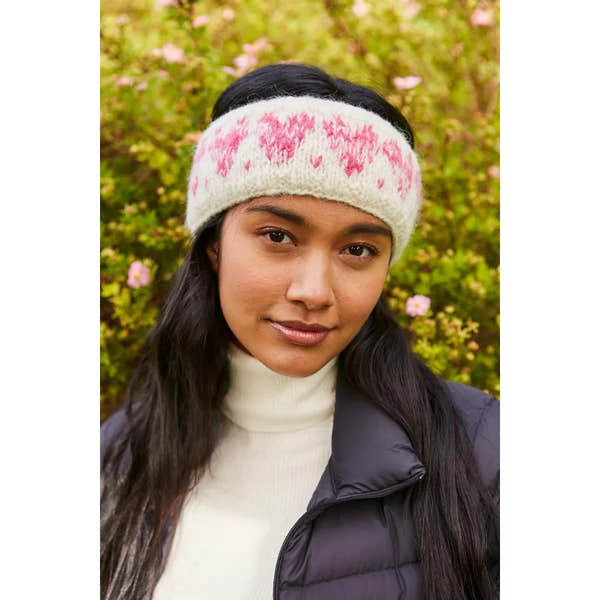 Pachamama Sweetheart Headband with pink heart pattern, knit fabric, worn by woman outdoors with floral background.