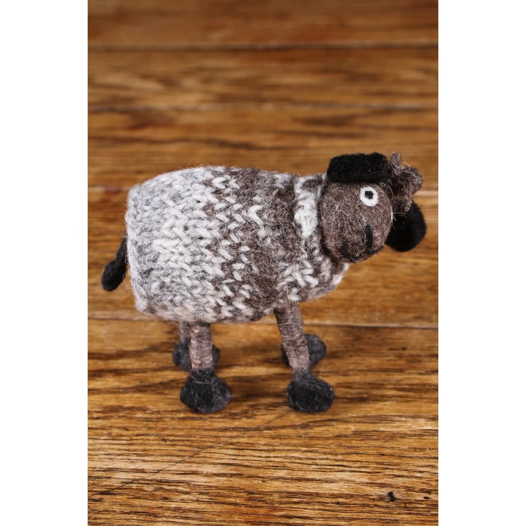 Felted wool Pachamama sheep figurine, gray and black with detailed features, on wooden surface.
