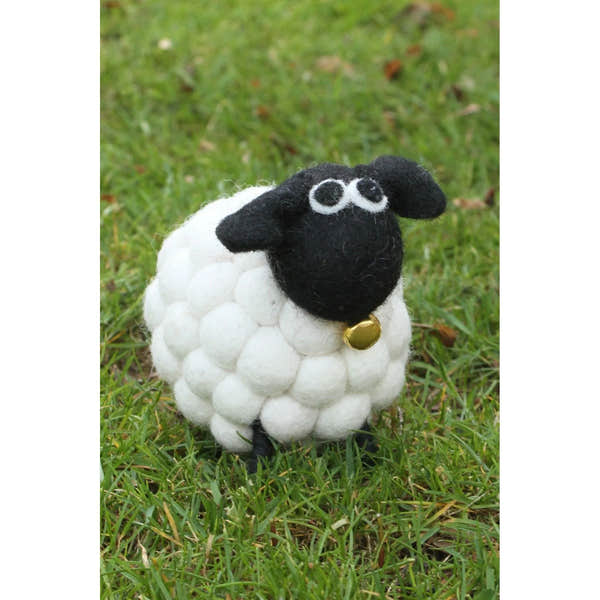 Cute felted sheep toy, "Tessa the Bobbly Lamb" by Pachamama, with a black face, ears, and gold bell, standing on grass.
