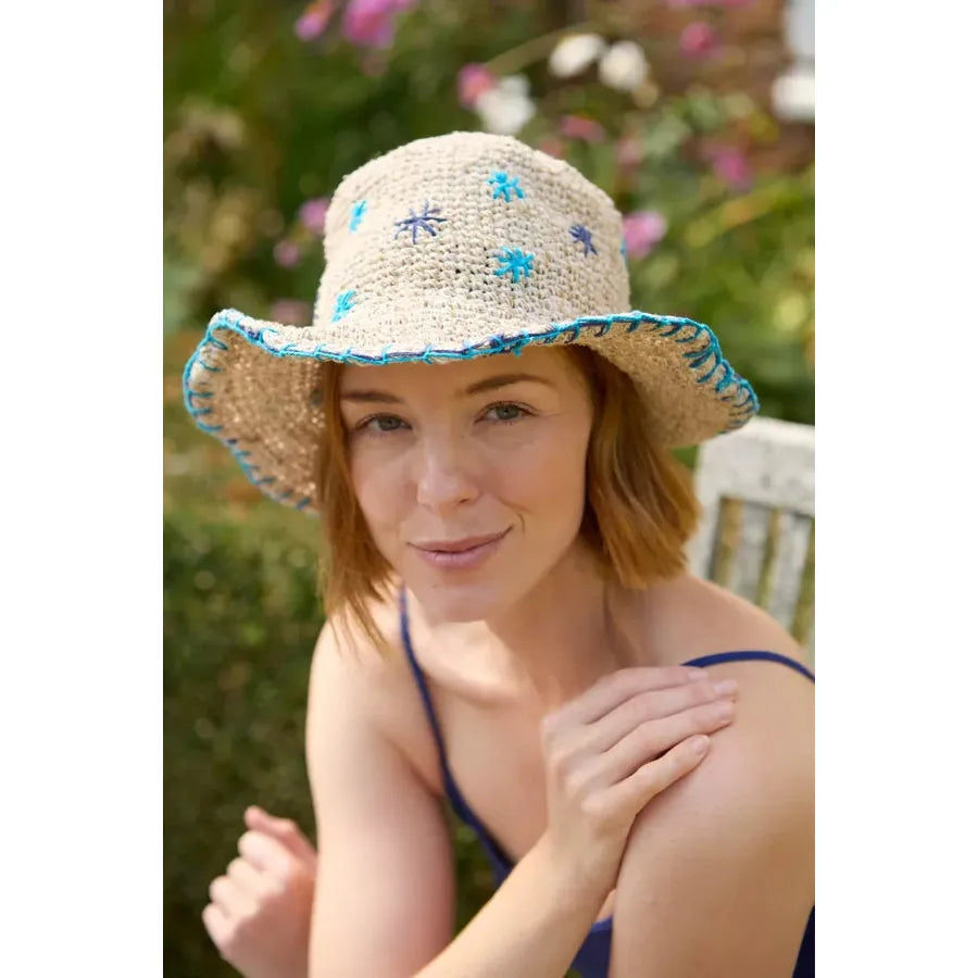 Pachamama wildflower hemp cotton hat in blue with embroidered flower patterns, worn by woman outdoors.