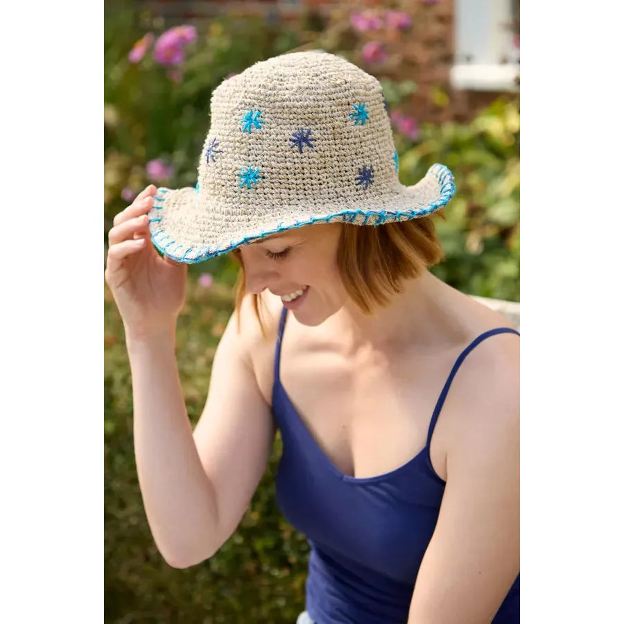 Woman wearing a blue Spachamama Wildflower Hemp/Cotton Hat with blue and teal embroidered flowers, outdoors in a garden.