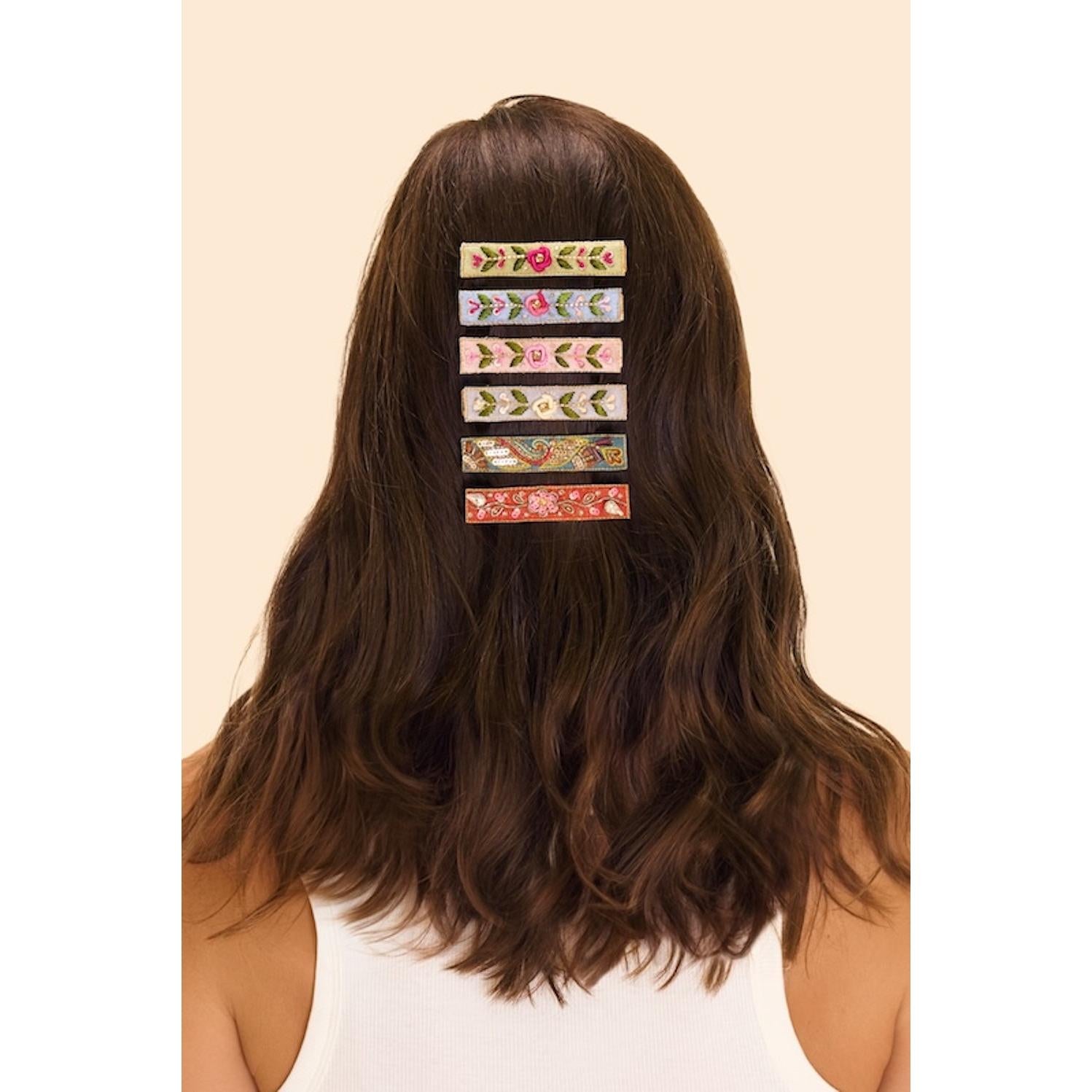 Powder narrow jeweled hair bar with floral petal and blue vine design, styled on brunette wavy hair.