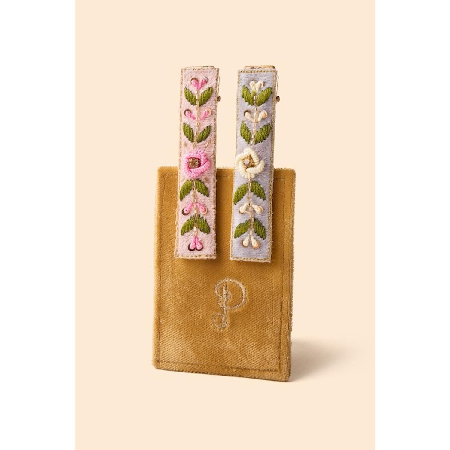 Powder narrow jeweled hair bar with pink and blue floral embroidery, set on a tan fabric pouch.