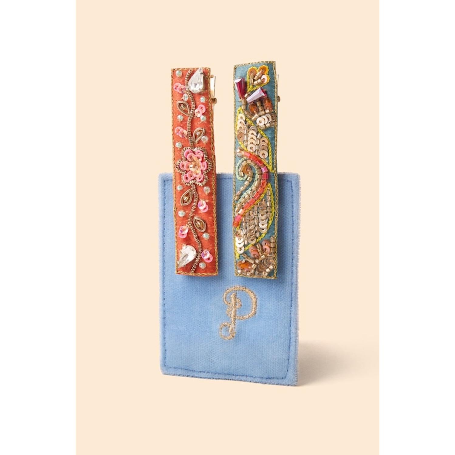 Powder narrow jeweled hair bar with orange floral and teal festival design, displayed on a blue velvet pouch.