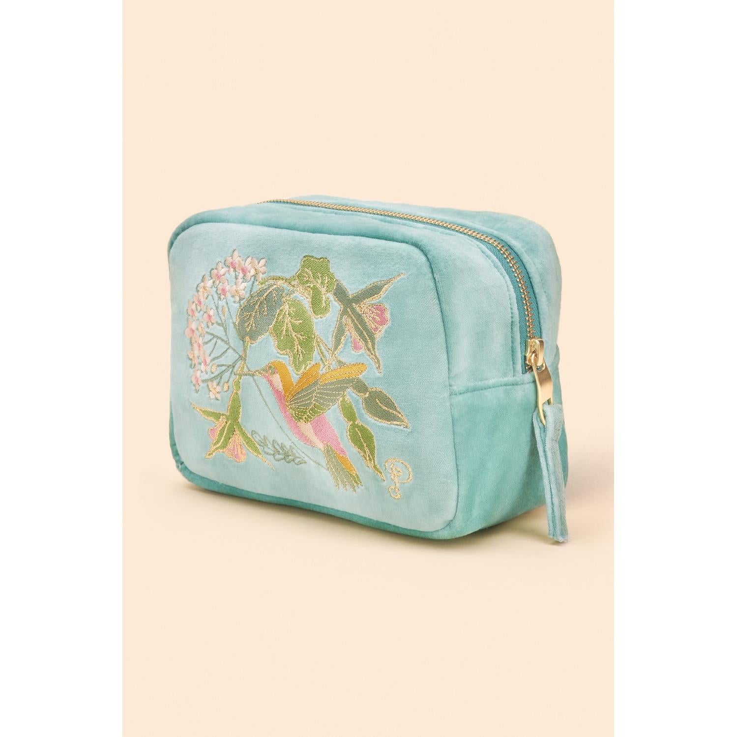 Powder velvet makeup bag featuring embroidered hummingbird and floral design, in soft blue with gold zipper detail.