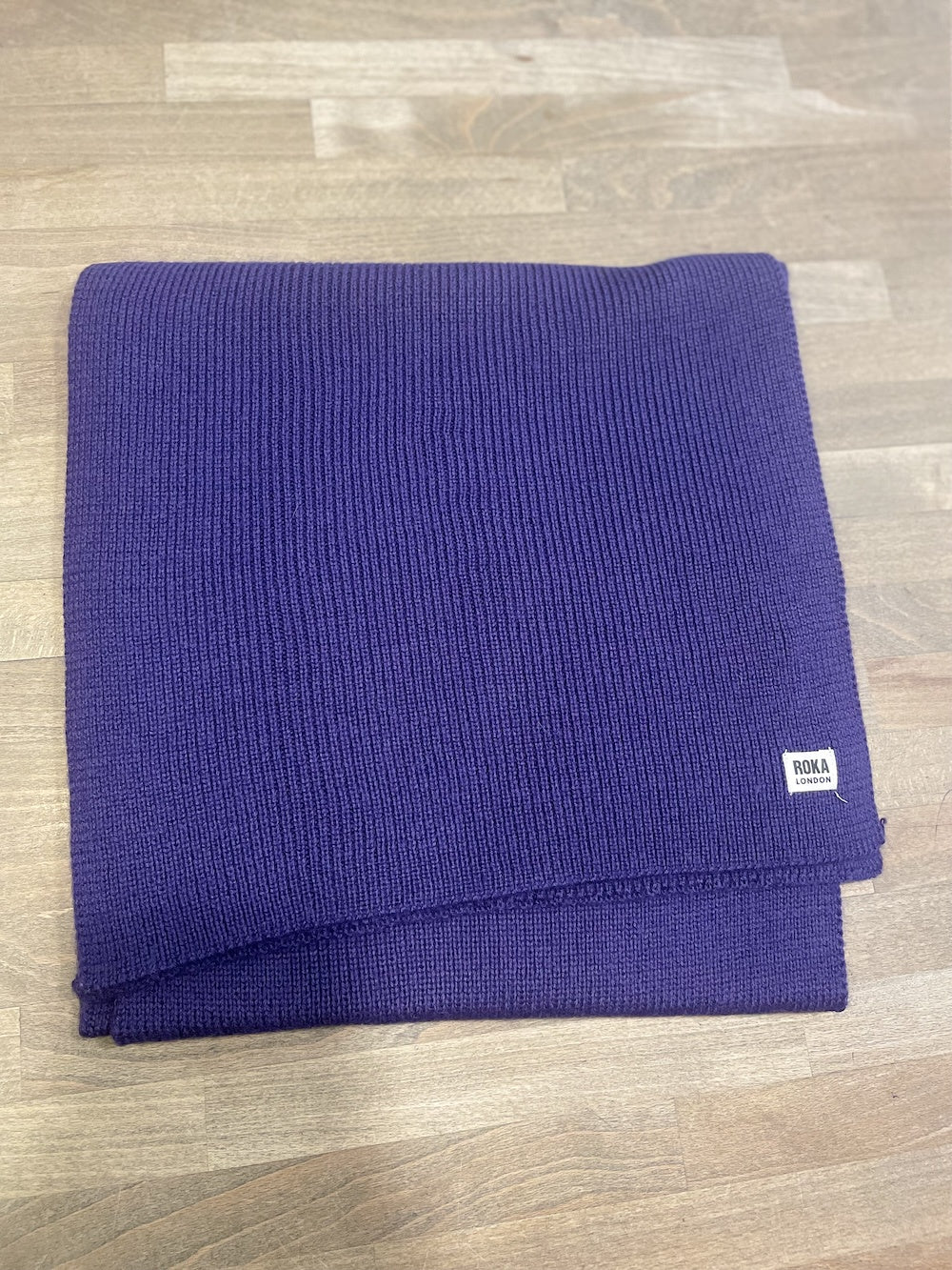 Royal purple ROKA London Hyde Peri scarf, ribbed knit fabric, folded neatly on wooden surface.