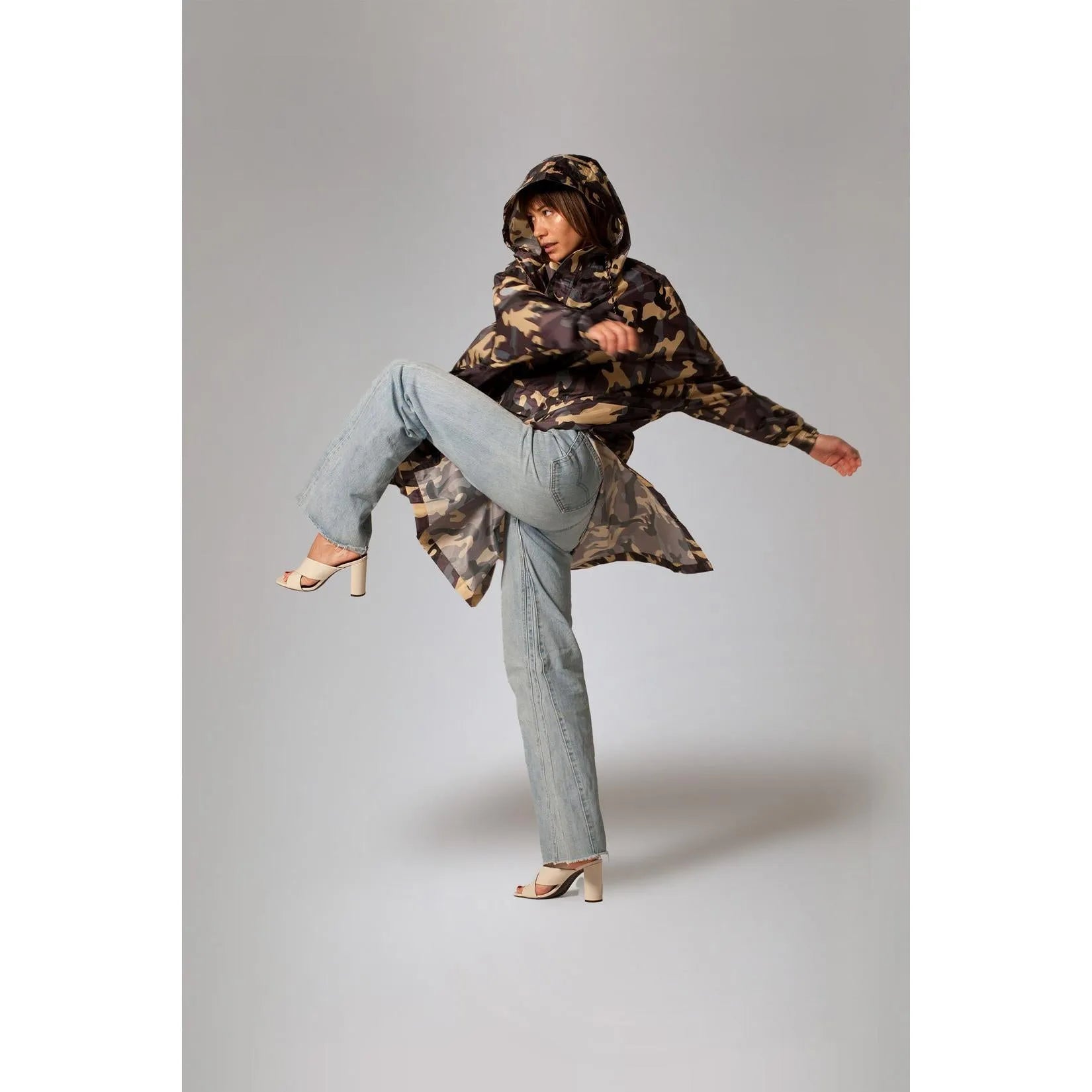 Rainkiss Camo Rain Poncho with hood, stylish camouflage pattern, oversized fit, paired with light blue jeans and heels.