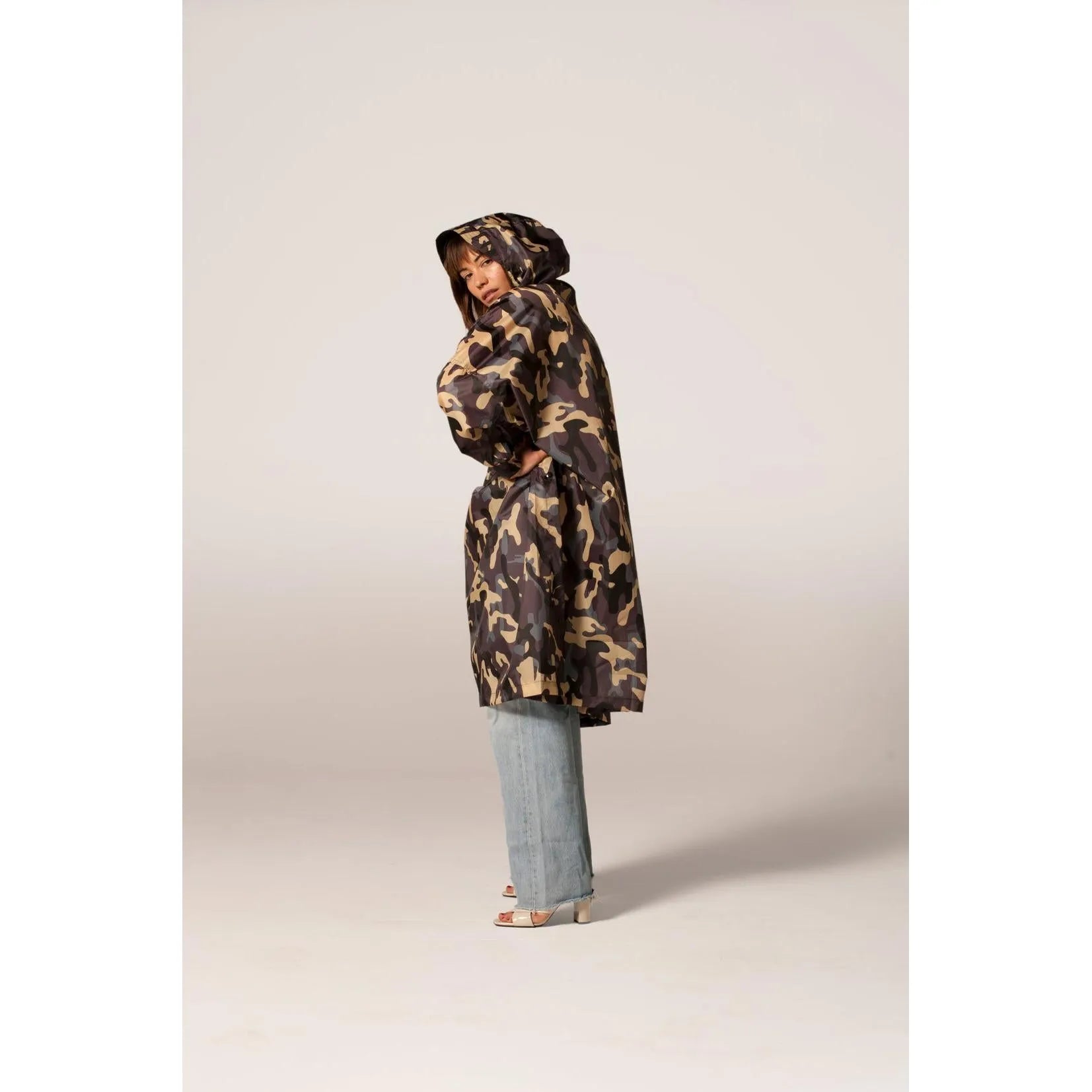 Rainkiss Camo rain poncho with hood, camouflage pattern, loose fit, and long length, styled with light wash jeans and heels.