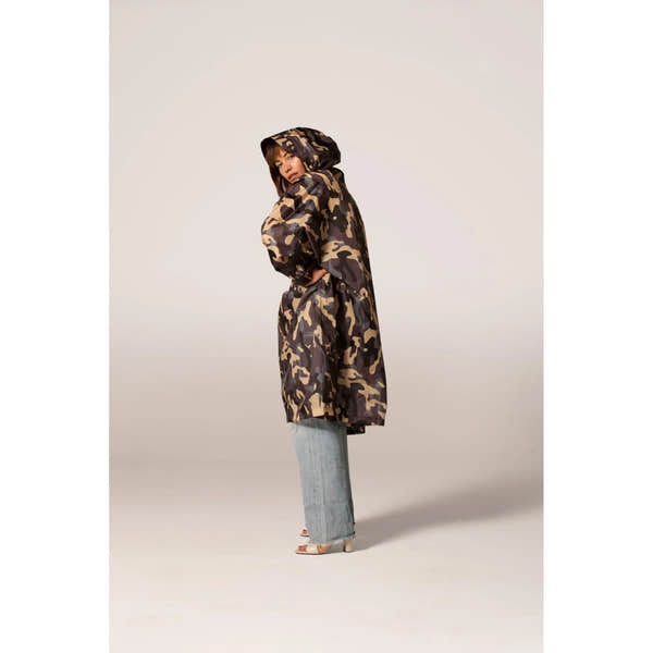 Rainkiss Camo rain poncho with hood, camouflage pattern, loose fit, and long length, styled with light wash jeans and heels.