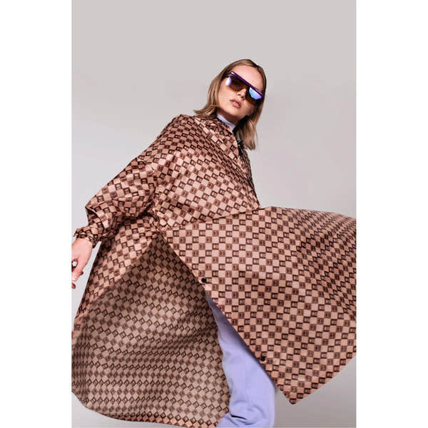 Rainkiss Damier rain poncho with a geometric checkered pattern, worn by a model with oversized sunglasses, stylish and waterproof.