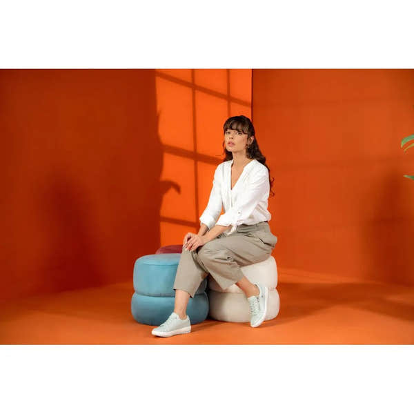 Lady wearing white shirt and beige pants sitting on colorful ottomans, showcasing mint leather water-resistant shoes.