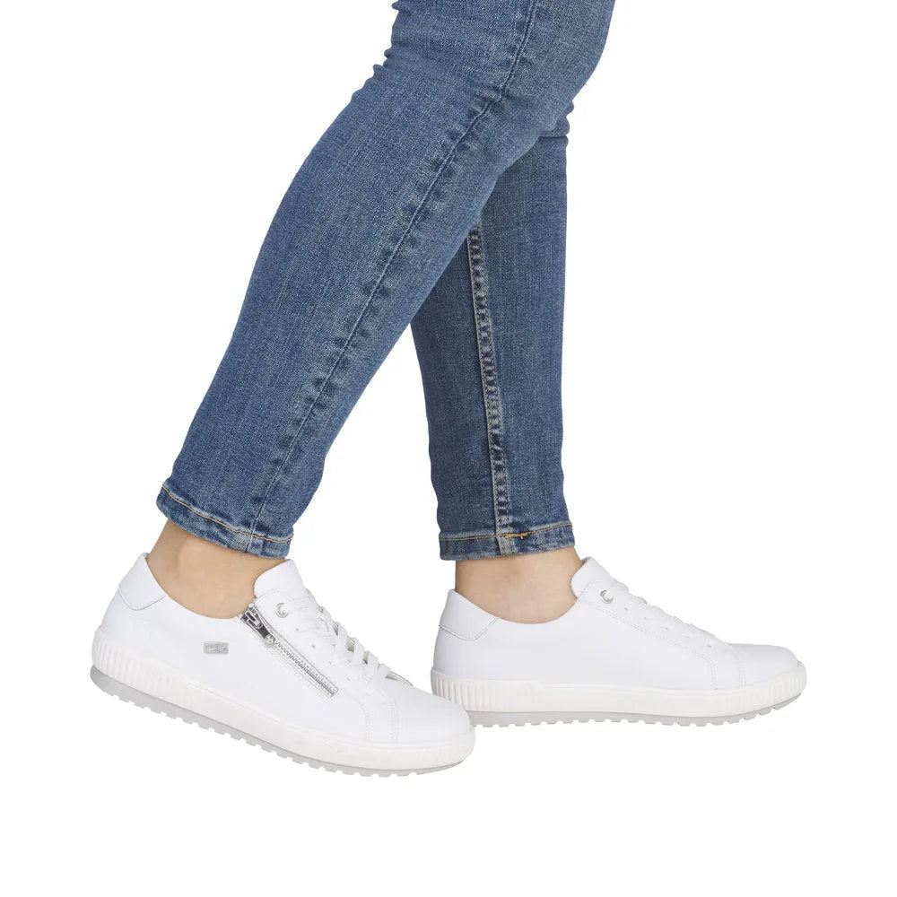 White leather sneakers with lace and zip closure, water-resistant, paired with blue skinny jeans. Stylish and comfortable.