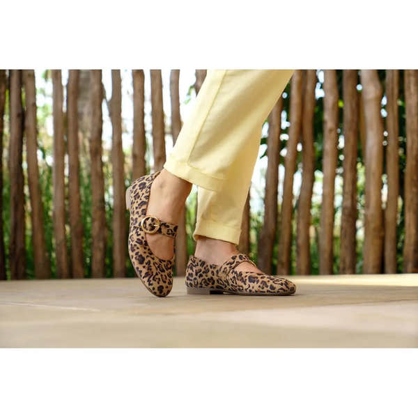 Leopard print suede touch fastening shoes with a gold buckle detail, worn with yellow pants on a wooden deck.