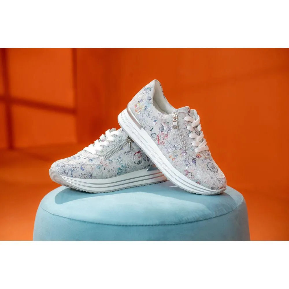 White floral printed suede sneakers with zip and lace details, chunky white sole, displayed on a light blue pedestal.