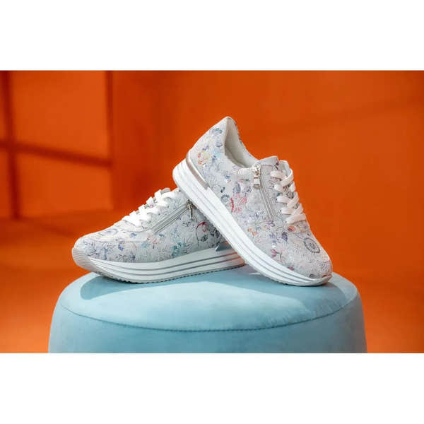 White floral printed suede sneakers with zip and lace details, chunky white sole, displayed on a light blue pedestal.