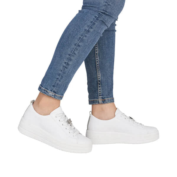 White leather lace-up shoes with chunky soles, worn with blue jeans.