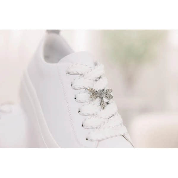 White leather lace-up shoe with a dragonfly charm on the laces, clean and minimalist style.