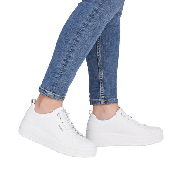 White leather lace-up shoes with thick soles worn with blue jeans, casual and stylish women's footwear.