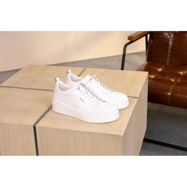 White leather lace-up sneakers with a thick sole, clean design, and minimal branding, displayed on a wooden table.