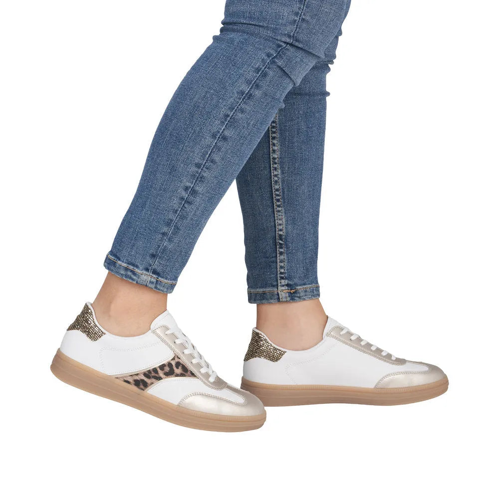 White and leopard lace-up trainers with gold accents and a textured sole, paired with denim.
