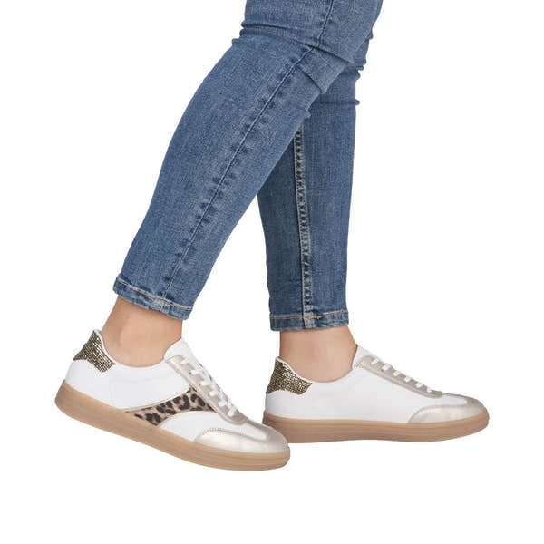 White and leopard lace-up trainers with gold accents and a textured sole, paired with denim.