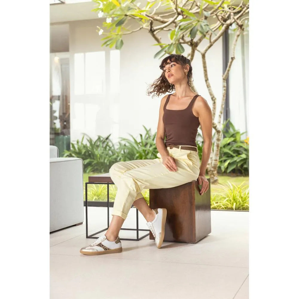 White and leopard print lace-up trainers with brown accents, displayed casually with a light outfit and natural greenery backdrop.