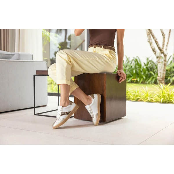 White and leopard lace-up trainers with beige accents, styled casually with light yellow pants in a bright setting.