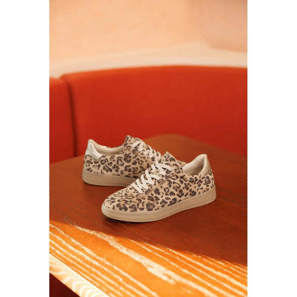 Leopard print sneakers on a wooden surface with an orange background