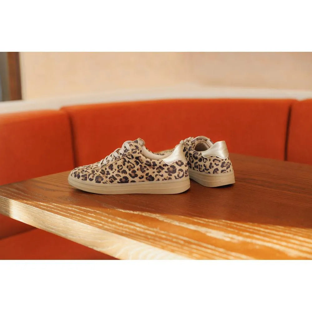 Leopard print sneakers on a wooden table with an orange couch in the background