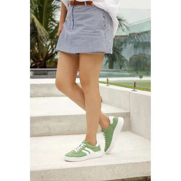 Green suede lace-up shoes with white soles, worn with a striped skirt and white top.