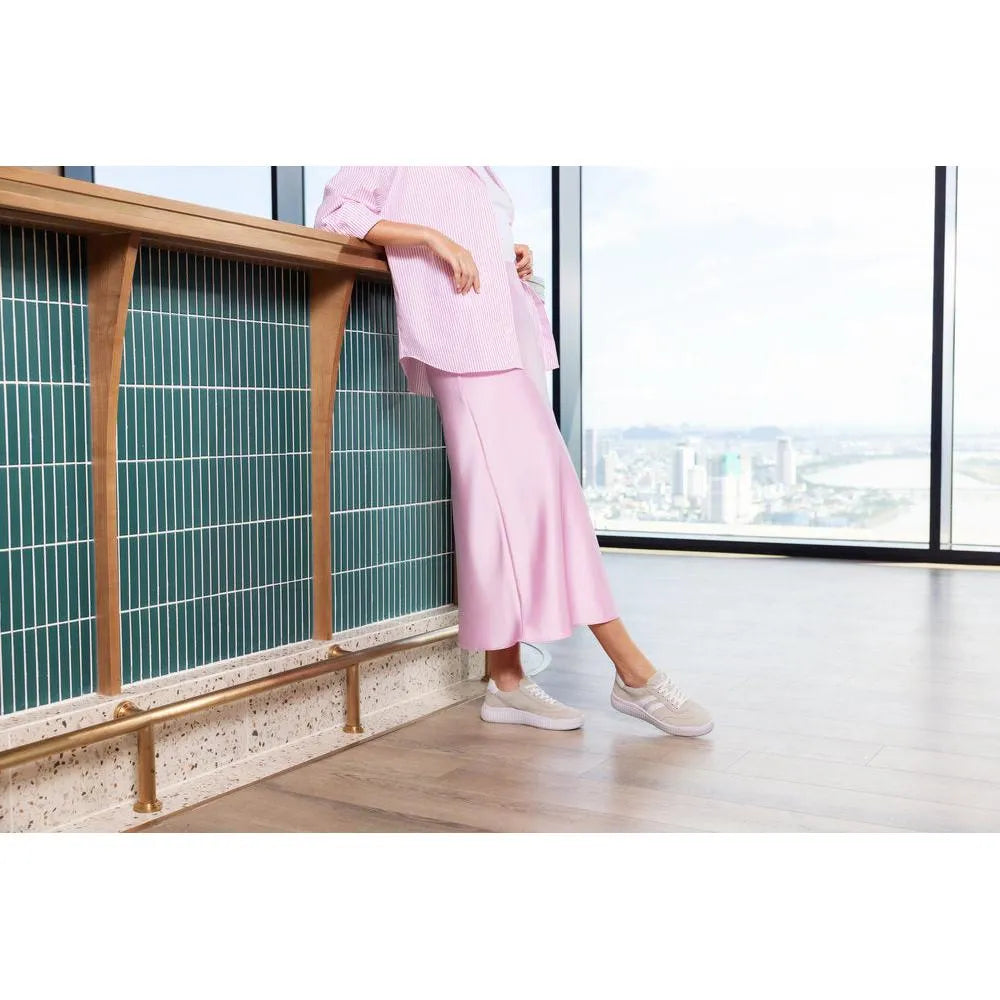 Beige suede lace-up shoes with a wide fit, worn by a person standing indoors with a city view background.