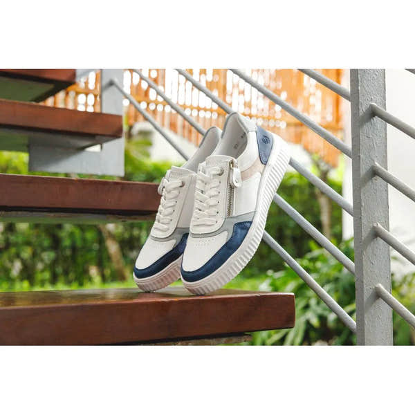 White, navy, and beige leather women's sneakers with zippers and laces, wide fit, stylish design, on wooden stairs.