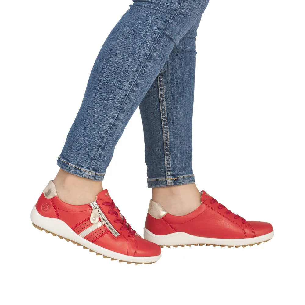 Women's red leather sneakers with side zipper, laces, beige accents, and white sole, paired with blue jeans.
