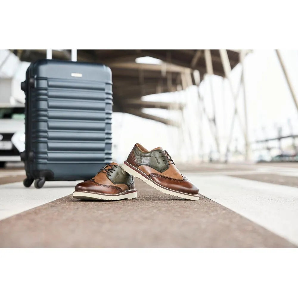 Rieker men's wide brown and green leather lace-up shoes with white sole, positioned on an airport floor near a blue suitcase.