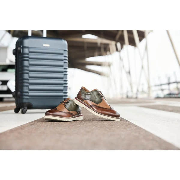 Rieker men's wide brown and green leather lace-up shoes with white sole, positioned on an airport floor near a blue suitcase.