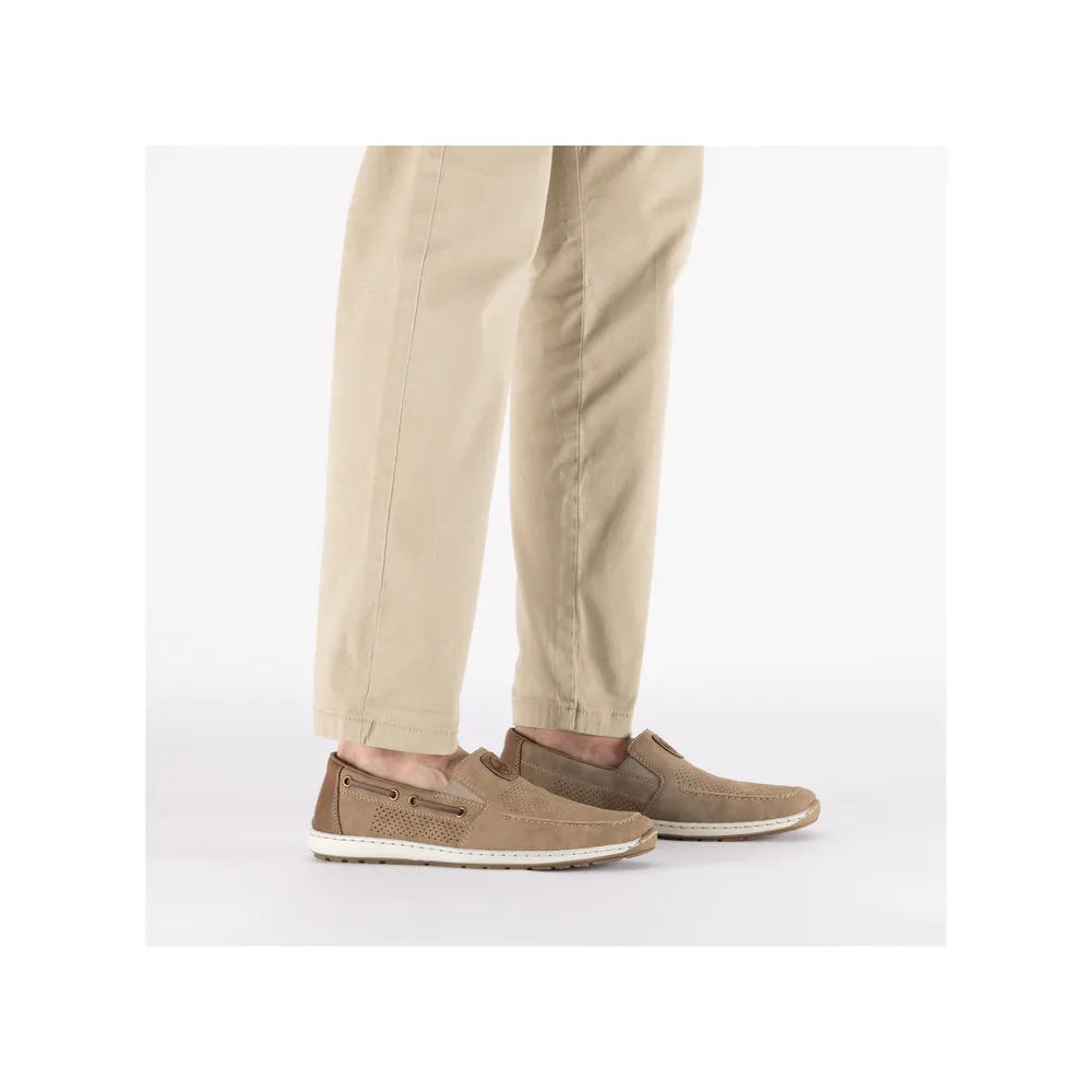 Beige slip-on deck shoes with perforated details and white rubber soles, worn with beige pants.