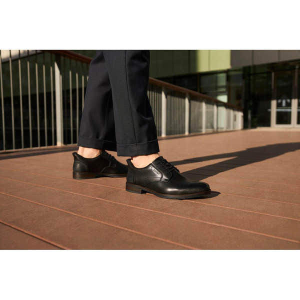 Rieker 10353-00 men's wide fit black leather slip-on shoes on a person walking outdoors.