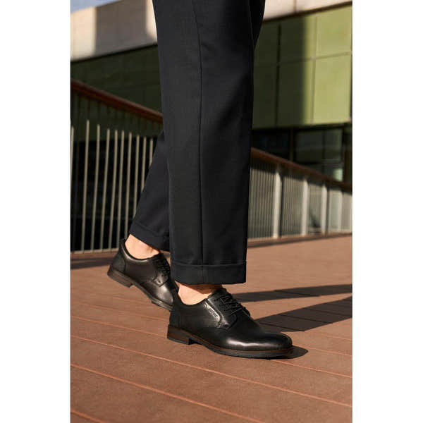 Rieker 10353-00 men's black leather slip-on shoes, wide fit, with laces and polished finish, worn on a wooden deck.