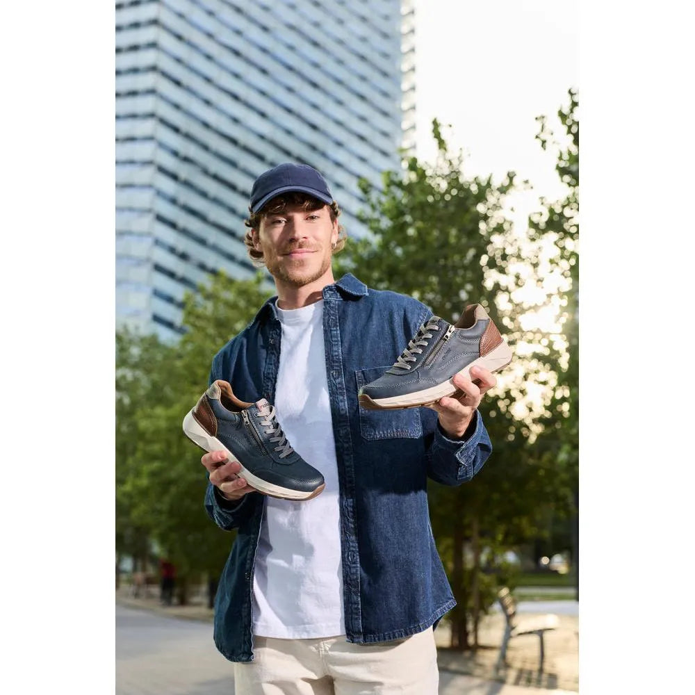 Man holding Rieker 11504-14 men's wide midnight zip and lace shoes outdoors, blue and brown materials, casual style.