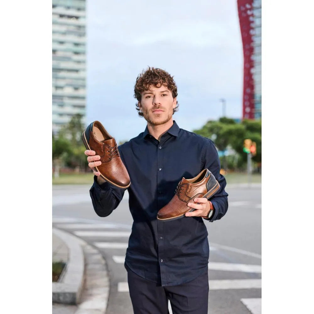 Man holding a pair of brown leather lace-up shoes outdoors in an urban setting.