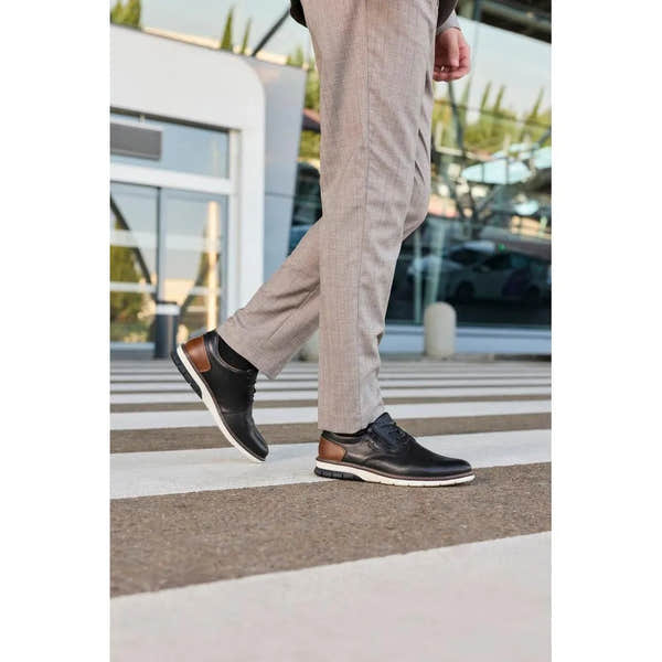 Men's black leather shoes with brown accents, lace-up and zip closure, sporty sole, worn with beige trousers.