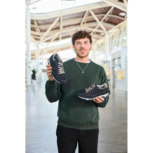 Man holds black navy leather lace-up shoes with gray accents at a modern, airy train station.