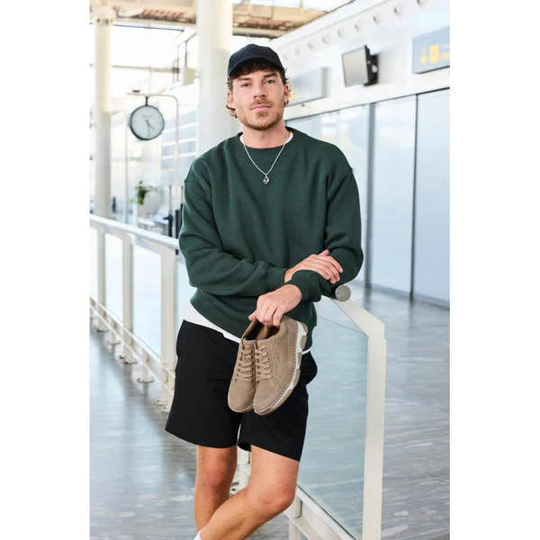 Men's wide brown leather lace-up shoes with a sleek design and sturdy sole, held by a man in casual attire at an airport.